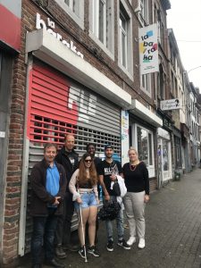 Jay with two people on her side is walking on a street in Liège souranded by buildings