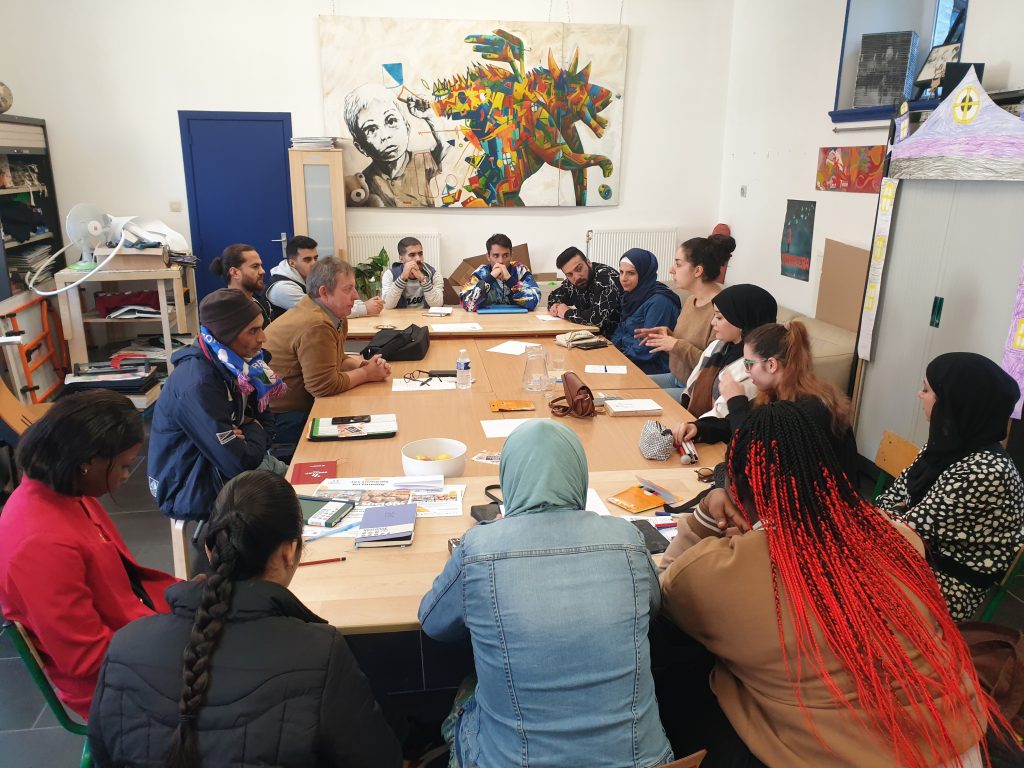 sixteen young people are gathered at a big table and are having a discussion