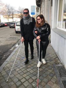 Jay and Mihai are walking on the street with their white canes. Mihai is blindfolded.