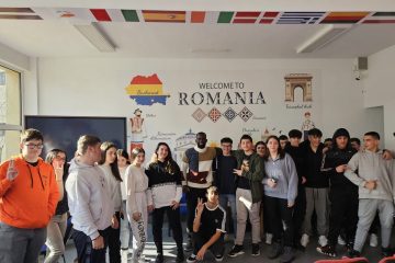 Anca, Abraham, the SAKURA NGO partners and numerous young volunteers pose all together in a room full of flags of European countries. On the wall behind them, the writing "Welcome to Romania"