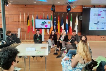 A group of young people sitting around a table. In the background a TV screen shows the LevelUP! 2024 logo.