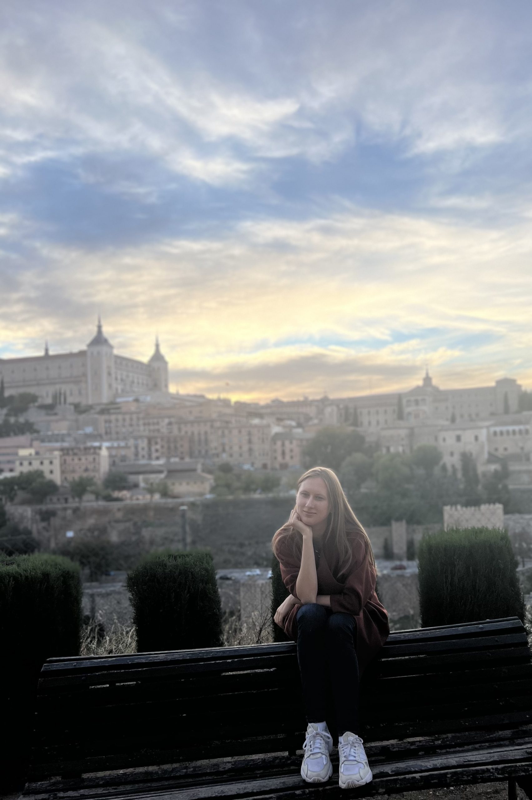 Kinga poses in front of a whimsical scenery in Spain, with the city of Toledo in the background.